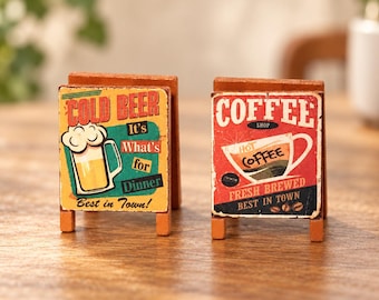 May include: Two miniature wooden A-frame signs. The left sign features a yellow beer mug graphic with the text COLD BEER It's What's for Dinner Best in Town! The right sign features a coffee cup graphic with the text COFFEE SHOP HOT COFFEE FRESH BREWED BEST IN TOWN.