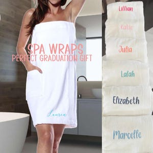May include: White spa wraps with the text "SPA WRAPS PERFECT GRADUATION GIFT". One wrap is worn, with "Lauren" embroidered on it. Several folded wraps are stacked, each with a different name embroidered in various colors.