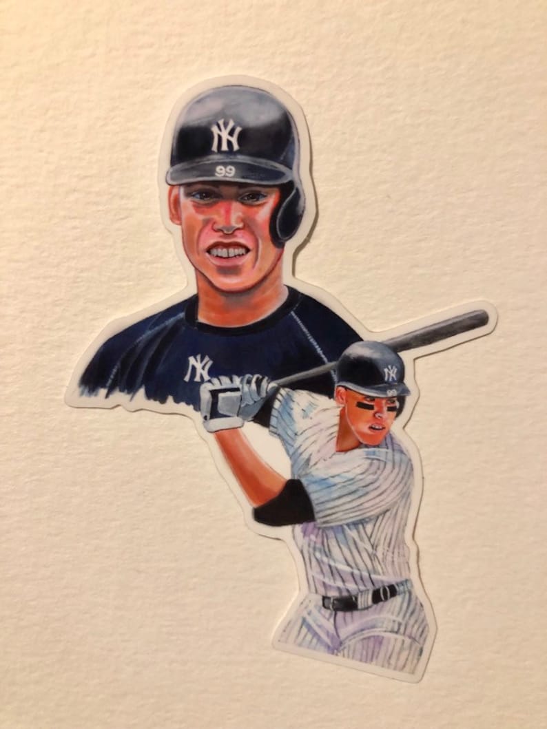 May include: A sticker featuring a baseball player wearing a New York Yankees uniform, holding a bat and swinging. The player is wearing a white and blue striped jersey with the team logo on the front. The player is also wearing a black helmet with the team logo on the front. The sticker is on a white background.
