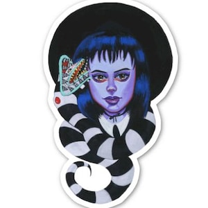 May include: A sticker featuring a cartoon illustration of a girl with black hair and a black hat. She is wearing a black and white striped dress and has a large, toothy, green creature behind her head.
