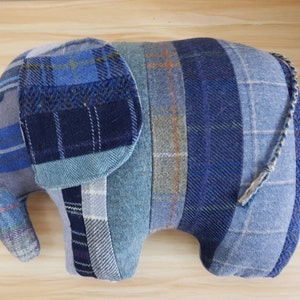 May include: A blue and gray patchwork elephant stuffed animal with a long tail. The elephant is made from different types of plaid fabric.