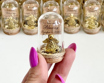May include: A miniature glass bottle with a cork stopper, filled with gold glitter and a gold angel ornament. The label reads "Naomi Blessing October 7, 2023". Other similar bottles are visible in the background.