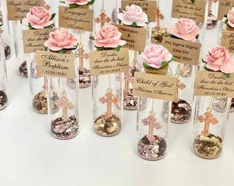 May include: A collection of small glass bottles filled with gold glitter and a small gold cross charm. Each bottle has a small tag with a personalised message and a pink flower.