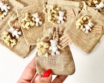 May include: A collection of small burlap bags with a teddy bear charm and dried flowers. Each bag has a personalized tag with the name "Angelina's" and the text "First Communion" and a date.