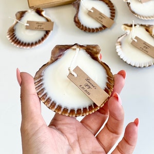 May include: A set of small, white, shell-shaped candles with brown edges. Each candle has a small, brown tag with white text that reads "Liam's Boy 6.30.2021".