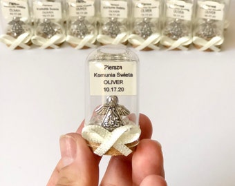 May include: A small glass bottle with a cork top and a white ribbon tied around it. Inside the bottle is a silver angel figurine. The bottle has a label that reads "Pierwsza Komunia Swieta OLIVER 10.17.20".