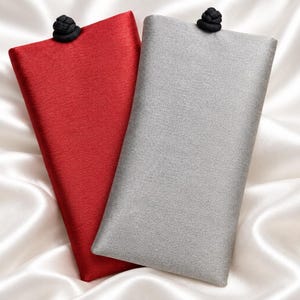 May include: Two rectangular fabric cases, one in deep red and one in light gray, each featuring a textured finish and a small black knot closure at the top center. The cases are positioned side by side, showcasing a clean, structured design.
