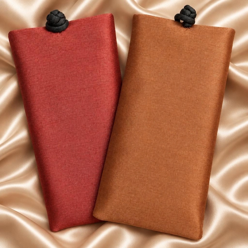 May include: Two rectangular fabric cases, one in deep red and one in warm brown, each featuring a textured surface and a small black knotted closure at the top center. The cases are positioned side by side, displaying a simple, flat design.