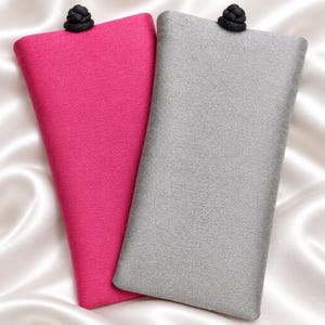 May include: Two rectangular fabric pouches, one in vibrant magenta and the other in light gray. Each pouch features a textured weave and is secured at the top center with a small, round, black decorative knot closure made of cord.