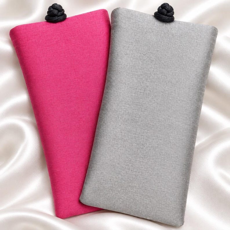 May include: Two rectangular fabric pouches, one in vibrant magenta and the other in light gray. Each pouch features a textured weave and is secured at the top center with a small, round, black decorative knot closure made of cord.