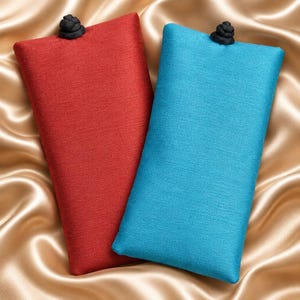 May include: Two rectangular fabric pouches, one in deep red and one in bright turquoise, each featuring a textured weave and a single black knotted button closure at the top center. The pouches are positioned side by side with a clean, flat design.