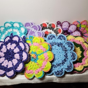 May include: A collection of ten crocheted flower-shaped pot holders in various colors, including purple, blue, green, pink, and white.