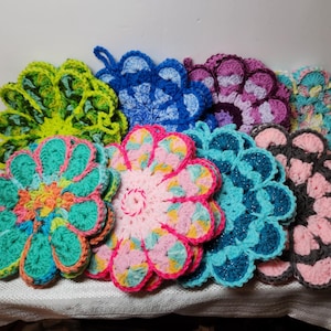 May include: A set of eight crocheted flower-shaped hot pads in various colors, including pink, blue, green, and purple. The hot pads are made with a variety of stitches and textures.