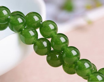 May include: A strand of green jade beads, strung together on a white surface. The beads are round and smooth, with a subtle sheen.