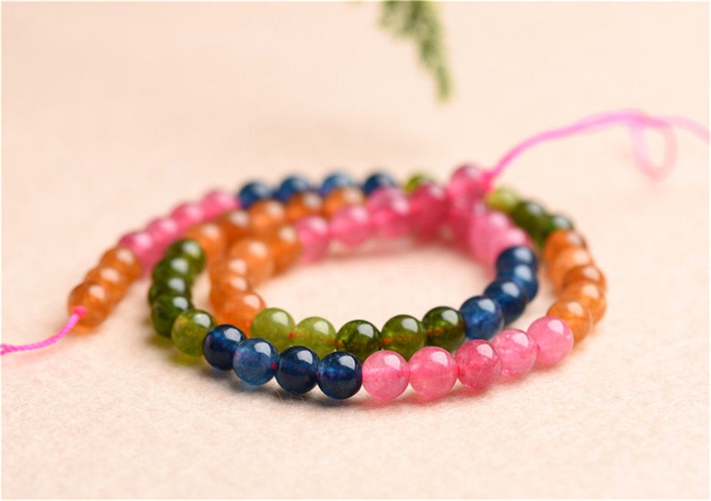 May include: A multi-coloured beaded necklace with pink, green, orange, and blue beads. The beads are round and have a smooth, polished finish.