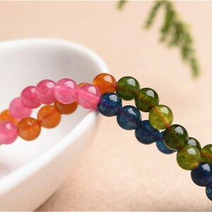 May include: A strand of round, colourful beads. The beads are pink, orange, blue, and green. The beads are strung on a clear thread.