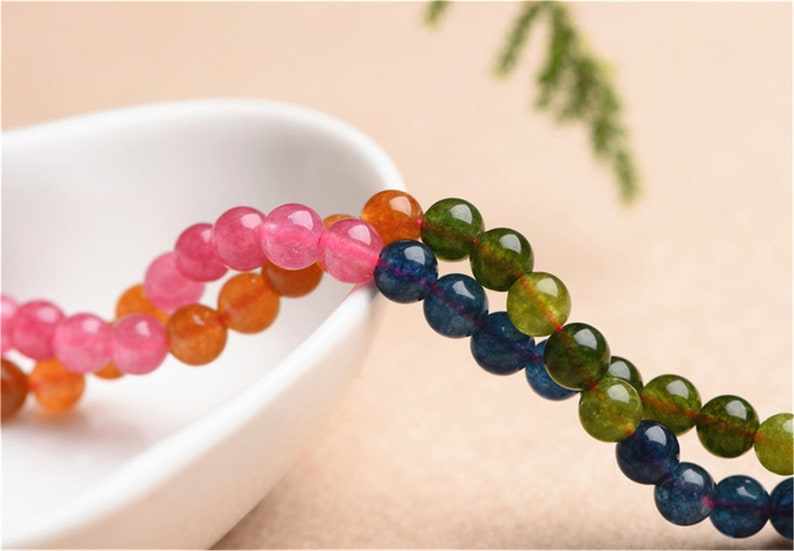 May include: A strand of round, colourful beads. The beads are pink, orange, blue, and green. The beads are strung on a clear thread.