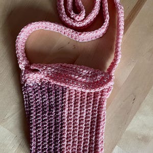 May include: A pink and purple ombre crocheted bag with a long pink crocheted strap.