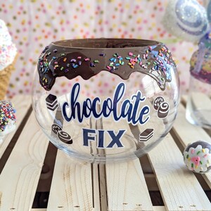 May include: A clear glass bowl with a chocolate rim and sprinkles. The bowl has the words "chocolate fix" written on it.