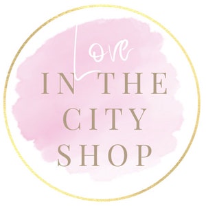 May include: A pink watercolor circle with a gold outline. The text "Love in the City Shop" is written in a brown font.