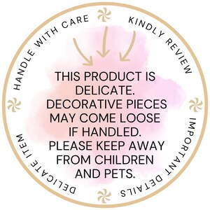 May include: A circular sticker with a beige border and a soft pink watercolor center. The text reads: HANDLE WITH CARE, KINDLY REVIEW, IMPORTANT DETAILS, DELICATE ITEM. Center text: THIS PRODUCT IS DELICATE. DECORATIVE PIECES MAY COME LOOSE IF HANDLED.