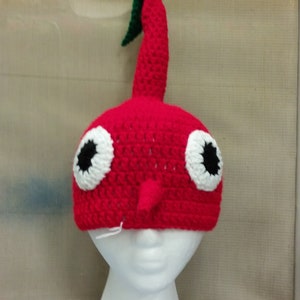 May include: Red crocheted hat shaped like a cherry with a green stem and white eyes with black pupils.