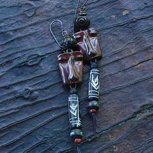 May include: A pair of long, dangling earrings with red and brown ceramic face-shaped charms, black and white patterned beads, and turquoise and red beads.