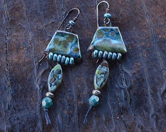 May include: Teal and green ceramic earrings with a geometric shape and bead accents. The earrings are suspended from a silver wire.