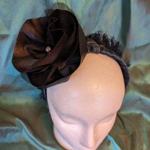 May include: A black fabric flower with a pearl center is attached to a denim headband.