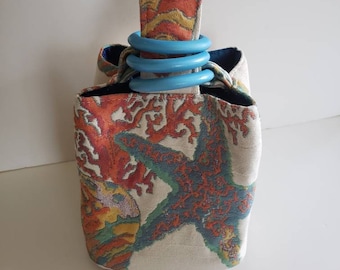 Reef Life Trio Bag showcases a weighty cotton woven with undersea beauty and lined in blue-green silk, enclosed by turquoise wooden rings.