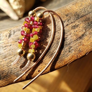 Może przedstawiać: Para złotych kolczyków koła z gromadą czerwonych i żółtych koralików z kamieni szlachetnych zwisających z każdego koła.