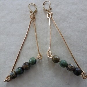 May include: Gold triangle shaped earrings with green and brown gemstone beads.