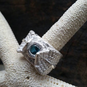 May include: A silver ring with a textured design and a blue gemstone set in the center.