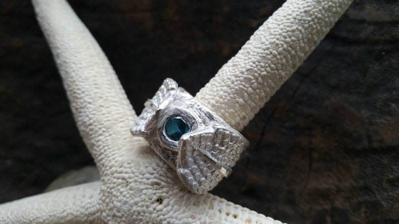 May include: A silver ring with a textured design and a blue gemstone set in the center.