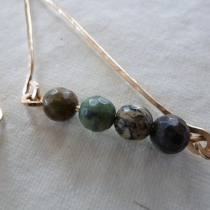 May include: Gold earrings with a geometric design featuring five green and brown gemstone beads.