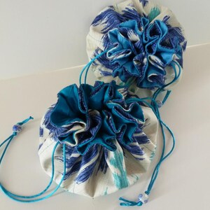 Op de afbeelding: Twee blauwe en witte trekkoordtassen met een gerimpelde rand. De tassen zijn gemaakt van een zachte stof met een bloemenpatroon.