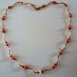 May include: A gold chain necklace with pink and red beads. The chain is wavy and the beads are round.