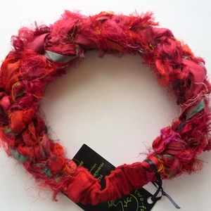 May include: A red, orange, and green silk ribbon headband. The headband is made of multiple strands of ribbon that have been frayed and twisted together. The headband is tied with a black ribbon.