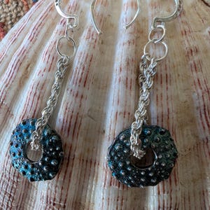May include: Silver earrings with a blue and black textured circular pendant. The pendant has a small hole in the center.