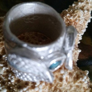 May include: A silver ring with a detailed design and a blue gemstone. The ring is sitting on a starfish.