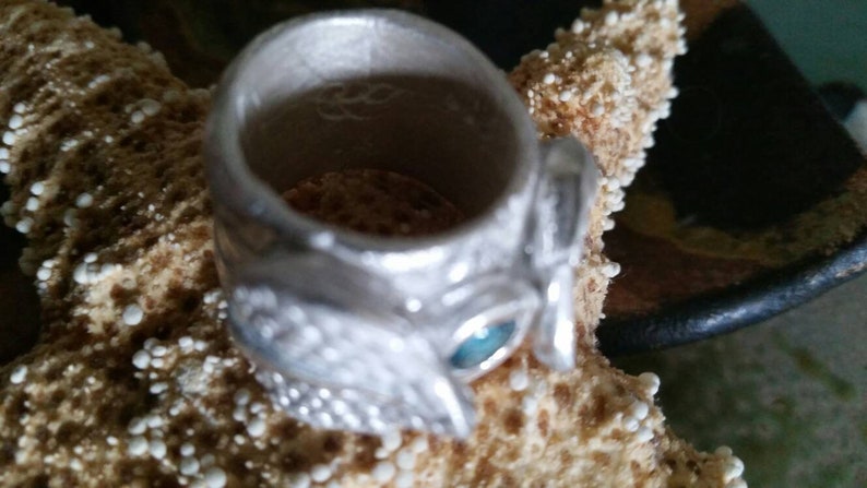 May include: A silver ring with a detailed design and a blue gemstone. The ring is sitting on a starfish.