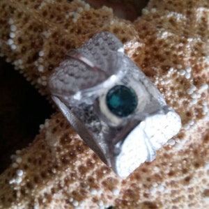 May include: A silver ring with a teal gemstone set in the center. The ring is decorated with a detailed design of leaves and swirls.
