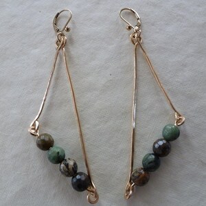 May include: A pair of gold triangle earrings with green and brown gemstone beads.