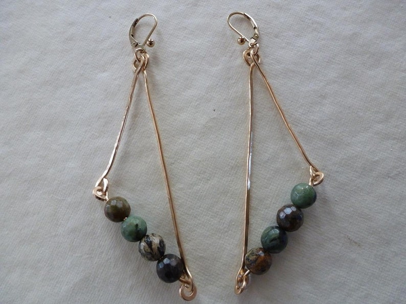 May include: A pair of gold triangle earrings with green and brown gemstone beads.