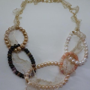 May include: A delicate necklace featuring a mix of pearls and beads in shades of pink, brown, and black. The necklace is adorned with a delicate gold chain and a layer of beige lace.