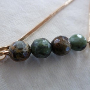 May include: A gold safety pin with four green and brown patterned beads attached.