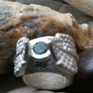 May include: A silver ring with a blue gemstone set in the center. The ring is decorated with intricate designs on the sides.