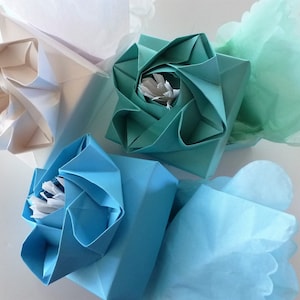 May include: Three origami flower boxes, one white, one teal, and one light blue, with tissue paper inside.