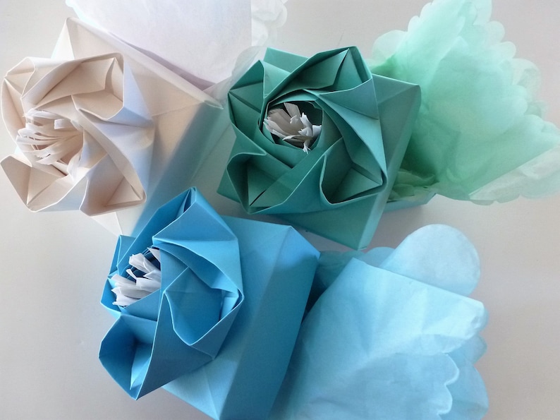 May include: Three origami flower boxes, one white, one teal, and one light blue, with tissue paper inside.