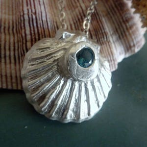 La collana Pendente in argento presenta un guscio di capesante e altamente dettagliato, montato con un topazio blu Londra. Una bellezza d'argento fine!